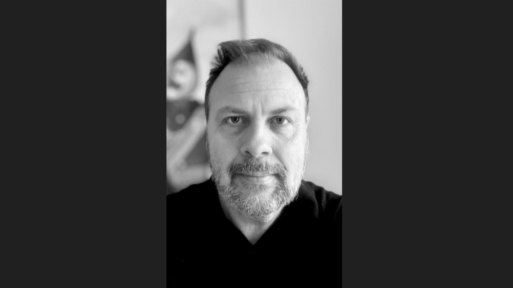 Sort hvidt portrætfoto af Sebastian Gyrst-Longsig Christensen. Han har kort hår og skæg.